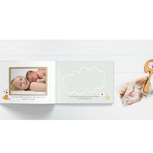 May include: A baby memory book with a light green cover and a cloud shape with lines for writing. The book has a photo of a baby and a sibling on the left page and a photo of a baby's feet on the right page. The book also has a small wooden rattle with a ball on the end.