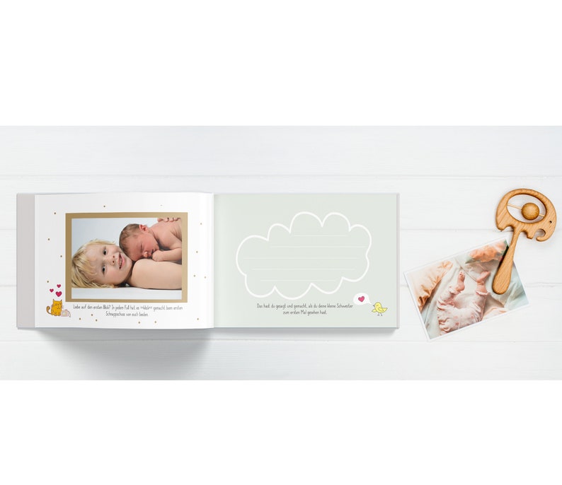May include: A baby memory book with a light green cover and a cloud shape with lines for writing. The book has a photo of a baby and a sibling on the left page and a photo of a baby's feet on the right page. The book also has a small wooden rattle with a ball on the end.