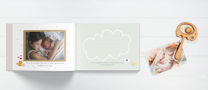 Op de afbeelding: Een baby-herinneringsboek met een lichtgrijze kaft en een witte wolk met lijnen om te schrijven. Het boek bevat een bruine foto van een jong meisje dat een baby vasthoudt. De tekst op de pagina luidt "Liebe auf den ersten Blick?"  "By you, I felt that I had a wonderful, precious little human being in my arms."  "Love at first sight?"  "By you, I felt that I had a wonderful, precious little human being in my arms."