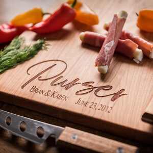 May include: Personalized wooden cutting board with the name "Purser" engraved in cursive, along with the names "Brian & Karen" and the date "June 23, 2012". The board has a built-in knife holder and a small knife.