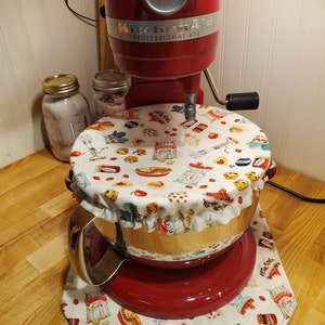 May include: A red KitchenAid Professional 600 stand mixer with a matching bowl cover and base mat. The cover and mat feature a white background with a repeating pattern of baking-themed illustrations, including flour bags, pies, and cookies.