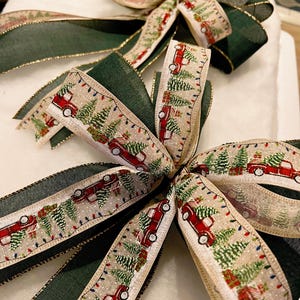 May include: A Christmas bow made with two types of ribbon. One ribbon is a green velvet ribbon with gold trim. The other ribbon is a beige ribbon with a repeating pattern of red pickup trucks carrying Christmas trees.