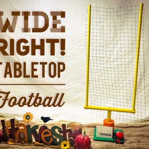 May include: A tabletop football goal made of yellow PVC pipe with a black net. The goal is set up on a brown surface with a fall-themed decoration in the foreground. The decoration includes a pumpkin, a sunflower, and the word "harvest" in colorful letters.