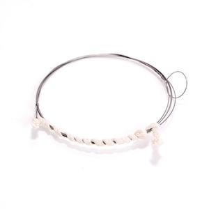 Könnte beinhalten: Nahaufnahme eines silbernen Drahtrings mit einem weißen Baumwollschnur umwickelt.