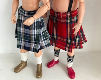 May include: Two male dolls wearing kilts. One kilt is green, white, and blue plaid, and the other is red, yellow, and black plaid. The dolls are shirtless and wear socks and shoes. One doll has short brown hair, and the other has long brown hair and a beard.
