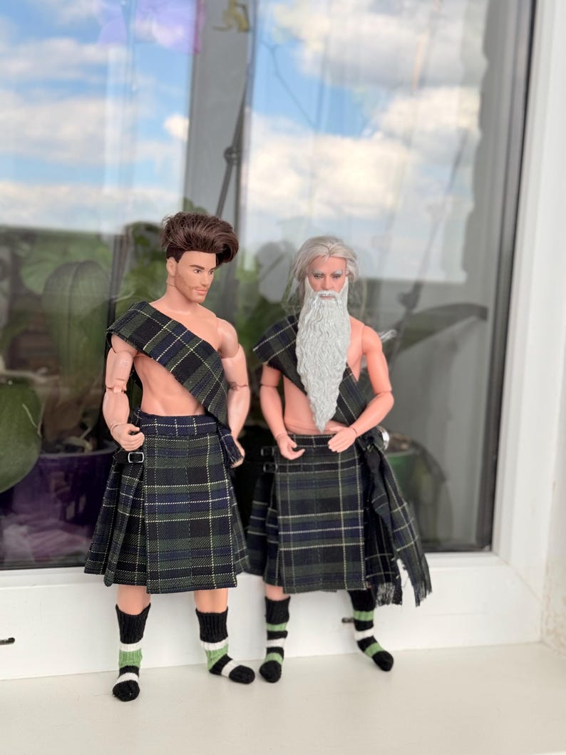 May include: Two male dolls wearing matching dark green, blue, and yellow plaid kilts and shoulder sashes. One doll has short brown hair, while the other has long gray hair and a long gray beard. Both dolls wear black, white, and green striped socks.