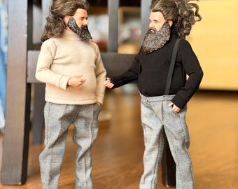 May include: Two male dolls with long brown hair and beards. One wears a beige turtleneck and gray plaid trousers with sneakers. The other wears a black turtleneck, black suspenders, gray plaid trousers, and black and white sneakers.