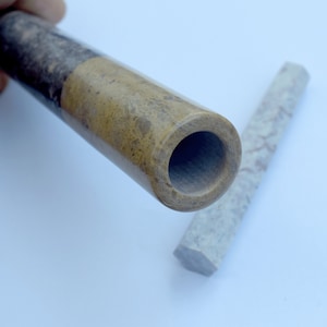 Può includere: Primo piano di una pipa da fumo in marmo marrone e nero con un'apertura rotonda. Una pipa di marmo grigio chiaro più piccola è sdraiata accanto.