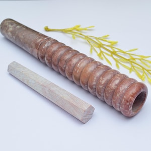 Könnte beinhalten: Ein brauner Holz-Nudelholz mit einer strukturierten Oberfläche und einem weißen Holzstift daneben.