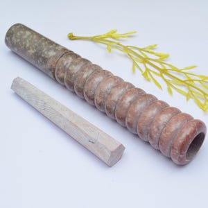 Può includere: Una pipa in marmo marrone e bianco con un'apertura rotonda e un tampone in legno separato. La pipa è realizzata in pietra naturale e ha una superficie unica e testurizzata.