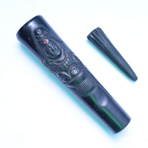 Puede incluir: Una pipa de fumar de madera negra con una imagen tallada de una deidad. La pipa tiene una pequeña boquilla de madera negra separada.