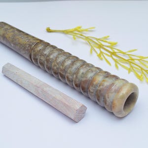 Könnte beinhalten: Eine braune und weiße Steinrolle mit einer strukturierten Oberfläche und einer runden Öffnung an einem Ende. Ein weißer Holzstab ist ebenfalls enthalten.