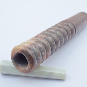 Könnte beinhalten: Eine braune und weiße Steinpfeife mit einem Spiralmuster. Die Pfeife liegt auf einem kleinen, weißen Stein.
