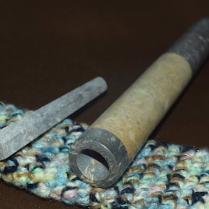 Op de afbeelding: Een set van twee stenen pijpen, een lange en een korte, met een gevlekte grijze en bruine kleur. De pijpen liggen op een kleurrijk gehaakt oppervlak.
