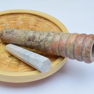 Può includere: Un set di due mortai e pestelli in pietra, uno marrone chiaro e uno grigio chiaro, che riposano in un cesto di bambù intrecciato.