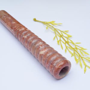 Op de afbeelding: Een rode en witte marmeren pijp met een spiraalvormig ontwerp. De pijp is ongeveer 25 cm lang en heeft een gladde, gepolijste afwerking.