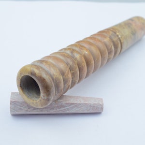 Può includere: Una pipa di pietra marrone e beige con un design a spirale. La pipa è appoggiata su una piccola pietra marrone chiaro.