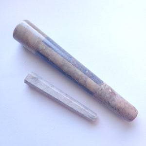 Può includere: Un set di due pipe da fumo in marmo grigio e bianco. La pipa più grande è più lunga e ha un diametro più ampio rispetto alla pipa più piccola.
