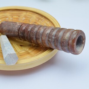 Può includere: Un mattarello di legno marrone con un cristallo esagonale bianco su un vassoio di bambù intrecciato.