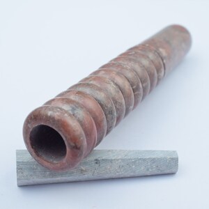Könnte beinhalten: Eine braune und graue spiralförmige Steinpfeife mit einem kleineren grauen Stein, der darauf liegt.