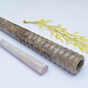 Könnte beinhalten: Eine braune und weiße Marmorpfeife mit einer runden Öffnung und einem Holzstift. Die Pfeife ist aus Naturstein gefertigt und hat eine einzigartige, strukturierte Oberfläche.