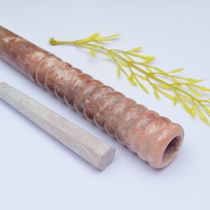 Könnte beinhalten: Eine braune und weiße Marmor-Rauchpfeife mit einem runden, hohlen Ende und einem kleineren, weißen Holzstößel. Die Pfeife hat eine strukturierte, gerippte Oberfläche.
