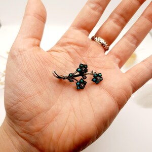 May include: A silver-toned floral brooch with turquoise and brown accents. The brooch features a delicate design of flowers and leaves, with small turquoise stones at the center of each flower.