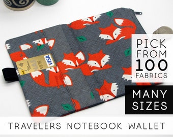 May include: A gray fabric wallet with a fox print and a zipper closure. The wallet has multiple card slots and a pocket for cash. The text "TRAVELERS NOTEBOOK WALLET" is printed on the bottom of the image. The text "PICK FROM 100 FABRICS" and "MANY SIZES" is printed on the right side of the image.