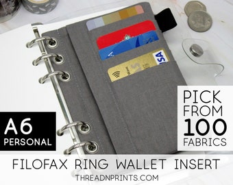 May include: A gray fabric wallet insert for a Filofax A6 personal size planner. The insert has three card slots and a clear plastic window for an ID card. The text "PICK FROM 100 FABRICS" is printed on the image.