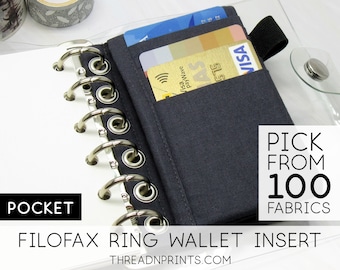 May include: A dark blue Filofax ring wallet insert with a pocket holding credit cards. The insert is next to a white notepad with silver rings. Text on the image reads "POCKET" and "PICK FROM 100 FABRICS".