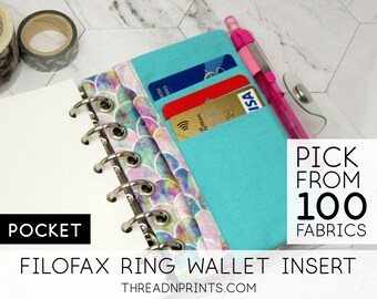 May include: A turquoise blue Filofax ring wallet insert with a pocket for cards and a pen. The insert has a colorful fabric with a mermaid scale pattern. The text "PICK FROM 100 FABRICS" and "FILOFAX RING WALLET INSERT" is printed on the image. The website address "THREADNPRINTS.COM" is also printed on the image.