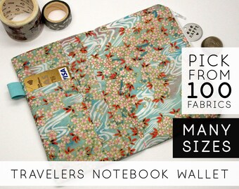 May include: A turquoise and white fabric wallet with a floral pattern and a zipper closure. The wallet has a pocket for a credit card and a strap for a pen. The text "PICK FROM 100 FABRICS MANY SIZES TRAVELERS NOTEBOOK WALLET" is printed on the image.