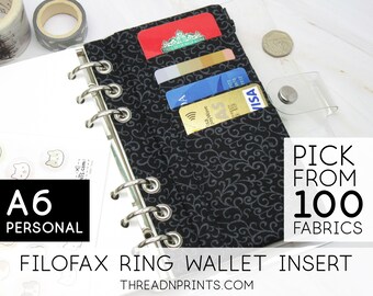 May include: A6 Personal Filofax ring wallet insert with a black fabric with a gray floral pattern. The insert has a clear plastic flap that holds cards. The text "PICK FROM 100 FABRICS" is visible in the image.
