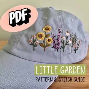 May include: A pale blue baseball cap featuring embroidered flowers, such as sunflowers and lavender. The text "LITTLE GARDEN PATTERN & STITCH GUIDE" is visible on the cap. A pink oval with the word "PDF" is in the upper left corner.