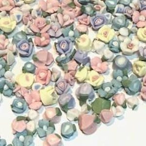 May include: Assortment of pastel-colored ceramic flower embellishments. The flowers are in various shapes and sizes, including roses, daisies, and other floral designs.