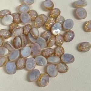 May include: A pile of small, oval-shaped, iridescent glass beads with a white and gold color scheme.