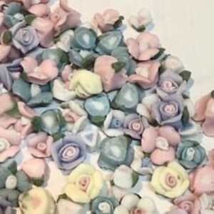 May include: Assortment of small ceramic flower embellishments in various pastel colors, including pink, blue, yellow, and purple. The flowers have a realistic appearance with delicate details.
