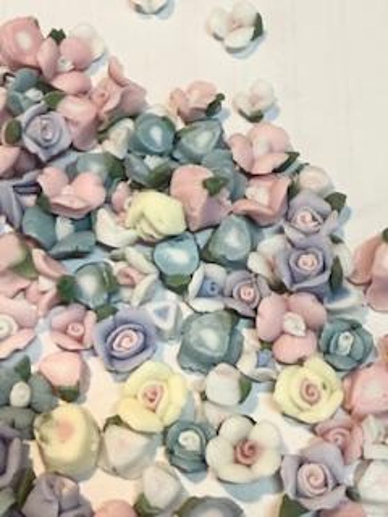 May include: Assortment of small ceramic flower embellishments in various pastel colors, including pink, blue, yellow, and purple. The flowers have a realistic appearance with delicate details.