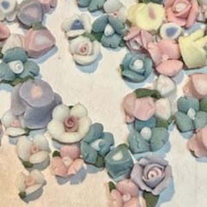 May include: Assortment of pastel-colored ceramic flower embellishments. The flowers are in various shapes and sizes, including roses, daisies, and other floral designs.