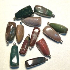 May include: Ten assorted agate gemstone pendants with silver-toned metal caps. The pendants are various shades of green, brown, red, and gray.