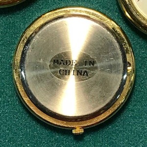 May include: Close-up of a gold-toned watch case with a silver-colored back. The back of the watch has the text "MADE IN CHINA" stamped on it. The watch case is round and has a gold-colored bezel.