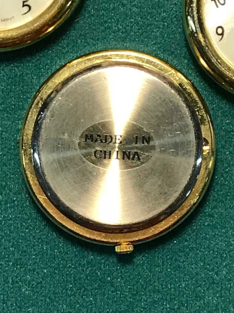 May include: Close-up of a gold-toned watch case with a silver-colored back. The back of the watch has the text "MADE IN CHINA" stamped on it. The watch case is round and has a gold-colored bezel.