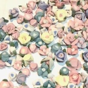 May include: Assortment of small ceramic flower embellishments in various pastel colors, including pink, blue, yellow, and white. The flowers are in different styles and sizes, with some featuring leaves.
