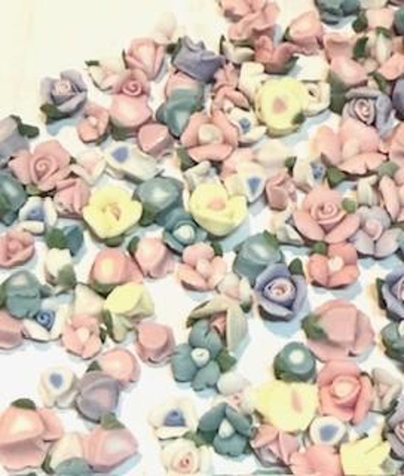 May include: Assortment of small ceramic flower embellishments in various pastel colors, including pink, blue, yellow, and white. The flowers are in different styles and sizes, with some featuring leaves.