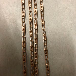 May include: Four gold chains with a linked pattern. The chains are laid out in parallel lines on a gray surface.