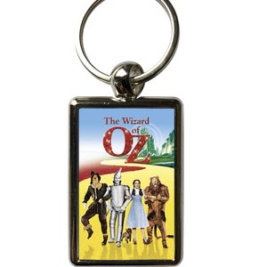 May include: A silver keychain with a rectangular metal charm featuring a colourful image of the characters from the Wizard of Oz film. The charm has the text "The Wizard of Oz" at the top and a large red "O" in the centre.