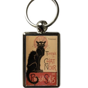 May include: A rectangular metal keychain with a vintage Le Chat Noir advertisement. The image depicts a black cat against a red and tan backdrop. The text "Tournée du Chat Noir de Rodolphe Salis" is displayed on the keychain.