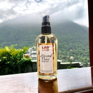 May include: A clear glass bottle with a black pump top and a white label. The label says "Lab Shaman Almond Elixir Body Oil 4 oz. Made with Almond Oil, Mineral Oil, Fragrance, Vitamin E & Love. Labshaman.com".
