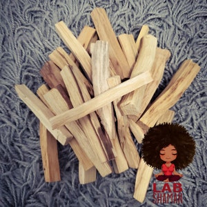 May include: A pile of light brown palo santo sticks on a gray fuzzy surface. The sticks are arranged in a random pattern. The image also includes a cartoon illustration of a person with curly hair sitting in a meditative pose. The text "LAB SHAMAN" is below the illustration.