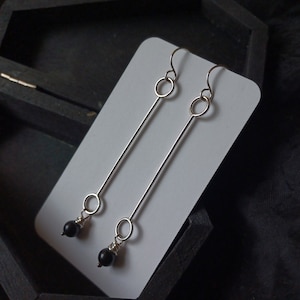 May include: A pair of silver dangle earrings with black beads and two silver circles on each earring.